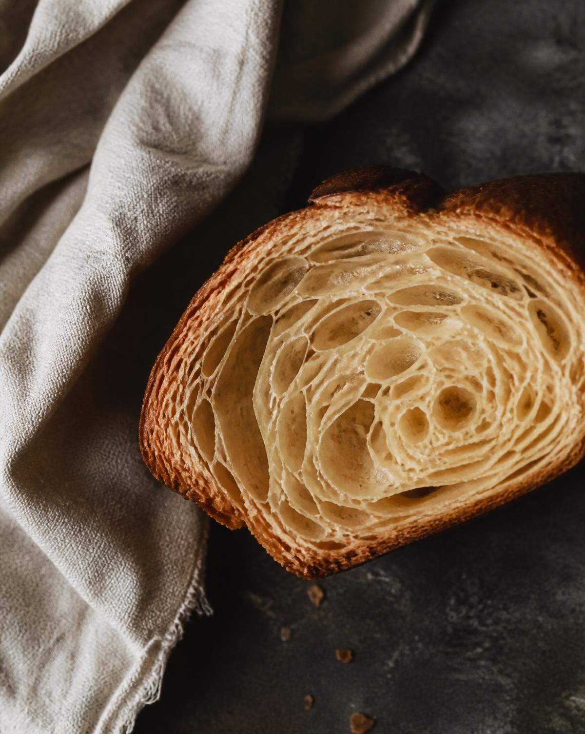 Cross-section of a laminated pastry on a dark stone counter beside a linen cloth.